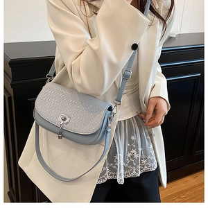 Détail d'un sac bandoulière bleu clair avec texture tressée et fermoir pivotant argenté
