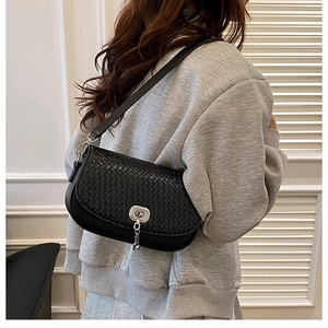 Mannequin portant un sac à bandoulière noir tressé avec boucle argentée dans un salon