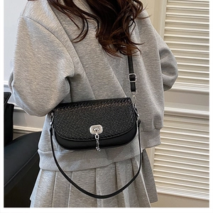Détail du sac bandoulière noir tressé avec fermoir rotatif argenté sur tenue grise