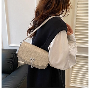 Détail du sac bandoulière tressé crème avec fermoir rotatif en métal et pompon décoratif