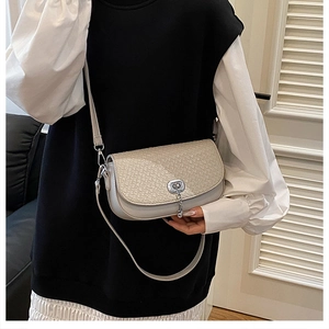 Mannequin portant un sac selle gris clair avec texture tissée et fermoir à chaîne