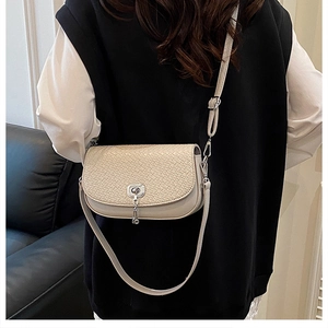 Détail du sac selle beige avec texture tressée et fermoir rotatif en métal argenté
