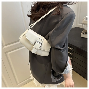 Detail shot of a cream leather shoulder bag featuring a prominent silver metal buckle strap