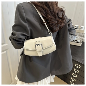 Detail of off-white leather saddle bag with silver buckle worn by model on shoulder
