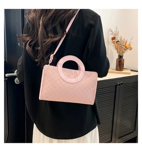 Rear view of a pink textured square crossbody bag with round handle on a white dress