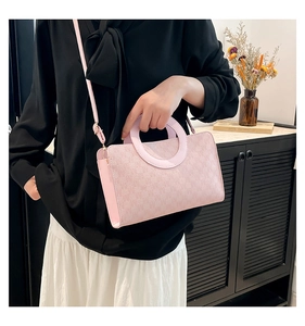 Detail view of pink textured faux leather crossbody bag with round handle and slim strap