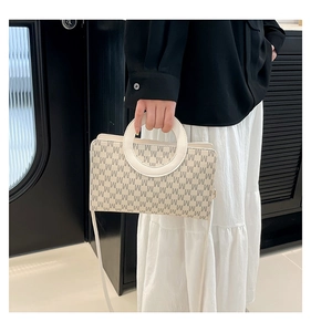 Close-up of the circular handle and M-letter print on the cream leather crossbody bag