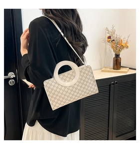Detail of beige monogram crossbody bag with white circular handle worn by a model