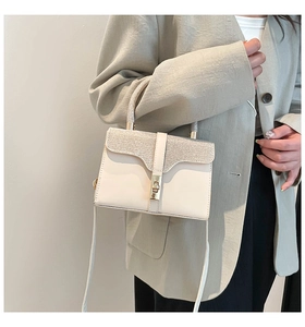 Close-up of white crossbody bag with rhinestone handle and silver metal lock detail