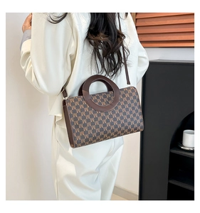 Detail of a brown leather bag featuring an M letter pattern and unique round cutout handle