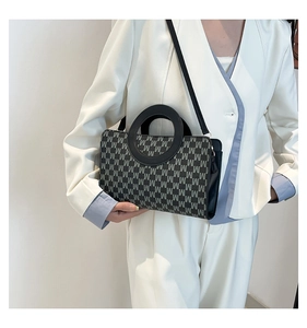 Detail of a chic handbag with monogram print and large circular handles worn with a blazer
