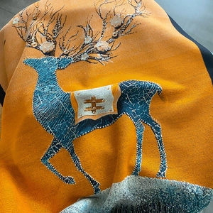 Detail of jacquard knit scarf showing a blue reindeer pattern on a vibrant orange fabric