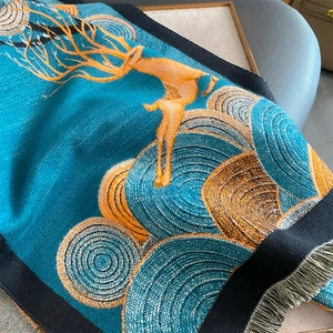Détail d'un châle en cachemire bleu sarcelle avec motifs d'élans dorés et franges