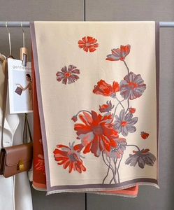 Detailed texture of beige cashmere-feel shawl featuring vibrant orange daisy patterns and tassels