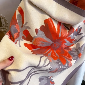 Close-up of thick beige cashmere scarf featuring orange floral patterns and fringed edges