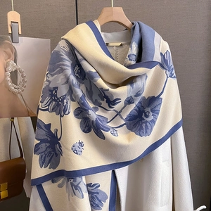 Thick winter cashmere scarf with blue floral print draped over a stylish white coat
