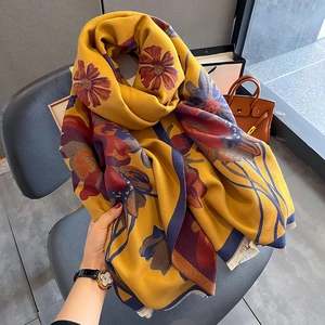 Detail of yellow cashmere-like scarf with blue floral prints and fringed edges