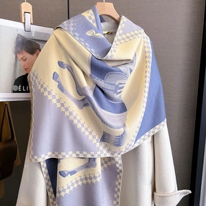 Detail of cashmere scarf showing blue horse pattern draped on white wool coat