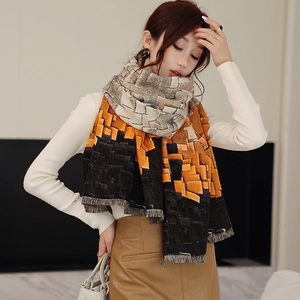 Detail view of jacquard woven plaid scarf with tassels in orange, black and beige
