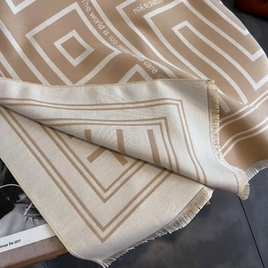 Detail of beige cashmere-like scarf showing Greek key patterns and fringe edges