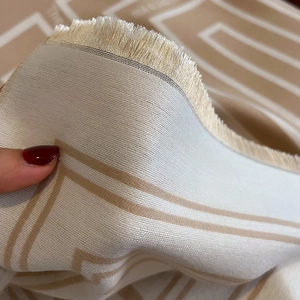 Macro shot of geometric beige woven scarf showing soft cashmere-like texture and neat tassels