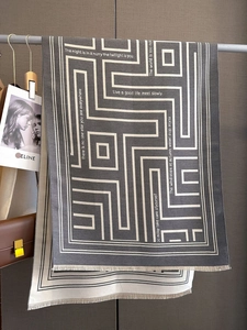 Detail of geometric letter print cashmere feel scarf with tassel edges and soft texture