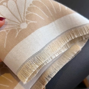 Detailed macro view of beige floral jacquard pattern and soft fringe tassels on scarf