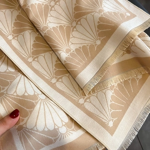 Detail shot of beige cashmere-feel scarf showing scallop jacquard patterns and tassels