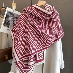 Nahaufnahme von rot-weißem geometrischem Strickschal mit weichen Fransen auf weißem Mantel