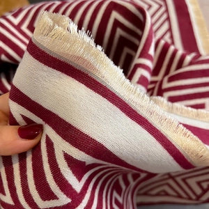 Detail eines geometrisch gestrickten Schals in Rot und Creme mit weichen Fransen