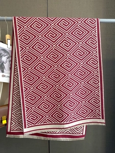 Detailansicht eines rot-beigen Strickschals mit geometrischem Muster und feinen Fransen