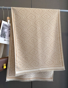 Detailansicht eines beigen Schals mit geometrischem Muster und Fransen auf grauem Hintergrund