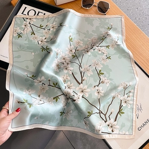Elegant silk scarf with white magnolia print in mint green, shown in a stylish flat lay setup