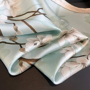 Close-up of silk scarf with magnolia pattern and premium champagne gold stitched edges