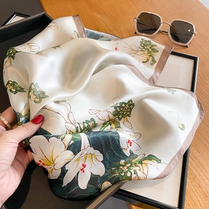 Silk square scarf with floral lily print and coffee brown hem on a wooden background