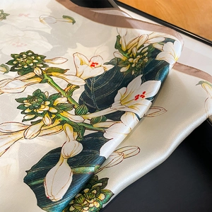 Elegant silk floral scarf with white lilies and green leaves on a folded luxury fabric