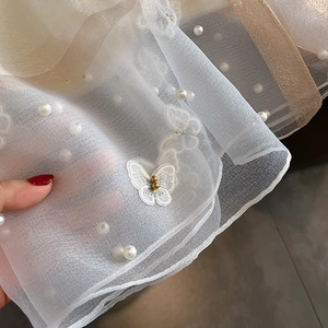 Détail d'une écharpe en soie avec broderie papillon blanche et perles décoratives