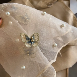 Détails de broderies papillons et perles blanches sur une écharpe en satin fin