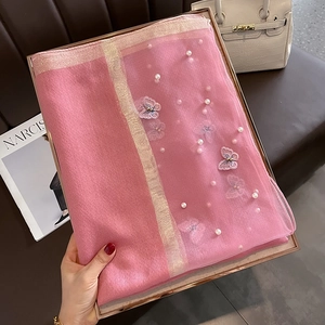 Détail d'une écharpe en soie rose avec broderie papillon et perles sur cuir marron