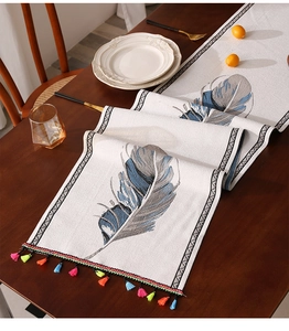 Detalle de camino de mesa bohemio con borlas de colores y estampado de plumas en lino
