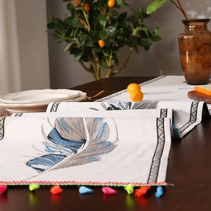 Camino de mesa bohemio con plumas azules y borlas de colores en una mesa de madera