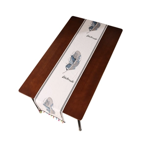 Camino de mesa moderno con plumas de acuarela y borlas de colores en mesa madera