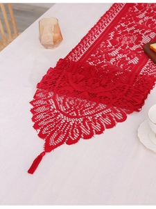 Close-up of red hollowed-out lace table runner with floral texture and tassel fringe