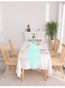 Macro detail of mint green lace table runner with hollow floral embroidery and tassels