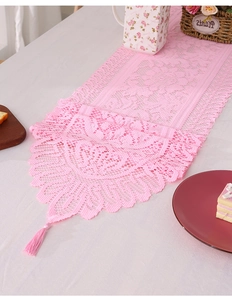 Close-up of pink lace table runner with hollow floral crochet patterns and tassel details