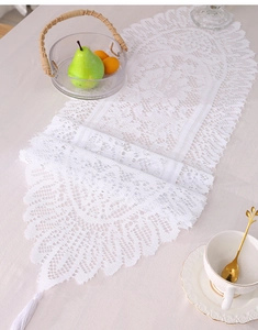 Close-up of white hollow lace table runner with floral texture and silk tassels