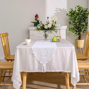 White lace table runner set with hollow floral patterns and fringe on white tablecloth