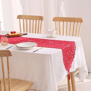 Red hollow lace table runner with fringe tassels on white tablecloth for dining decor