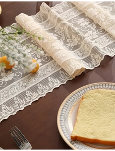 Detail of vintage white lace table runner with hollow floral patterns and fringe on wood