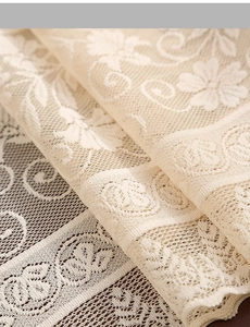 Macro view of beige hollow lace fabric featuring intricate floral crochet patterns and fringe